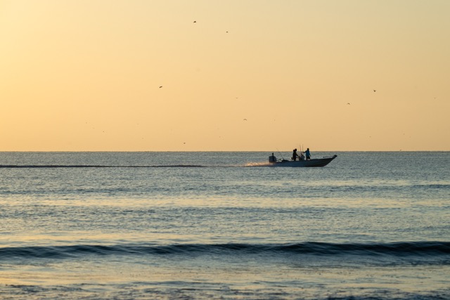 AfishingboatspeedsdownthecoastatsunriseintheAtlanticOceanofftheshoreofJettyParksbeachaccess
